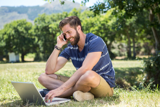 坐在草地上用笔记本电脑的男人