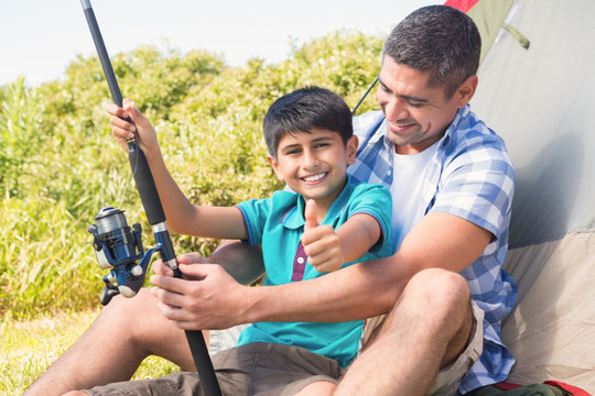 坐在帐篷前教儿子用钓鱼竿的父亲