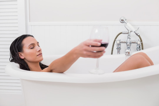 躺在浴缸里拿着一杯红酒的女人