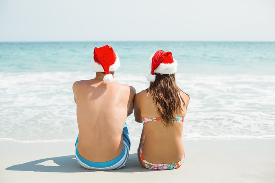 戴着圣诞帽坐在沙滩上的夫妇