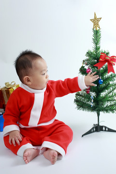 穿圣诞服装尝试去摸圣诞树婴儿