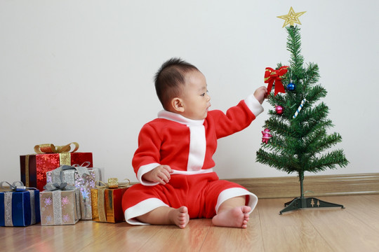 穿圣诞服装坐木地板抓圣诞树婴儿