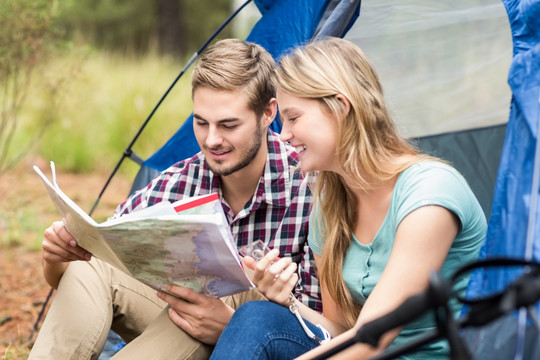 年轻的夫妇坐在帐篷里看地图