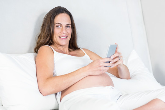 坐在床上使用手机的孕妇