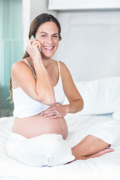 坐在床上使用手机打电话的孕妇