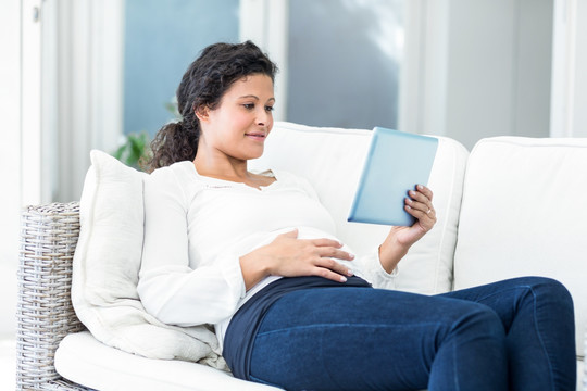 躺在沙发上使用平板电脑的孕妇