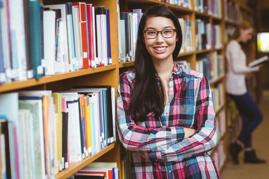 微笑的大学生靠在图书馆书架上