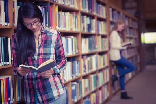 微笑的学生靠在书架上看书