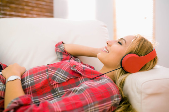 漂亮的金发美女躺在沙发上听音乐