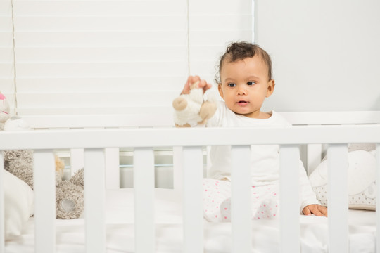 可爱的婴儿在婴儿床上玩毛绒玩具