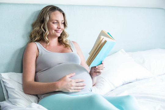 怀孕的女人躺在她的床上看书