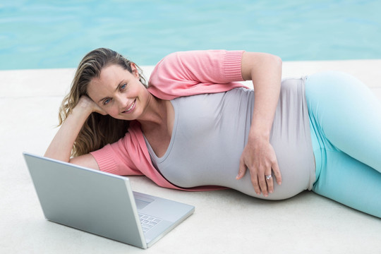在泳池边用笔记本电脑的孕妇