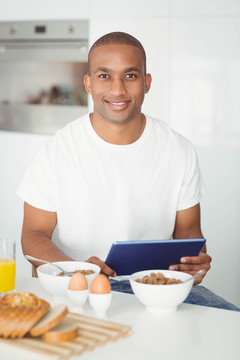 年轻人使用平板电脑在厨房吃早餐