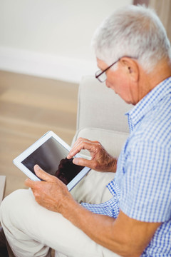 坐在沙发上使用平板电脑的老人