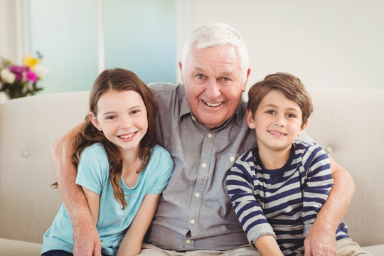 微笑祖父和孙子孙女坐在沙发上