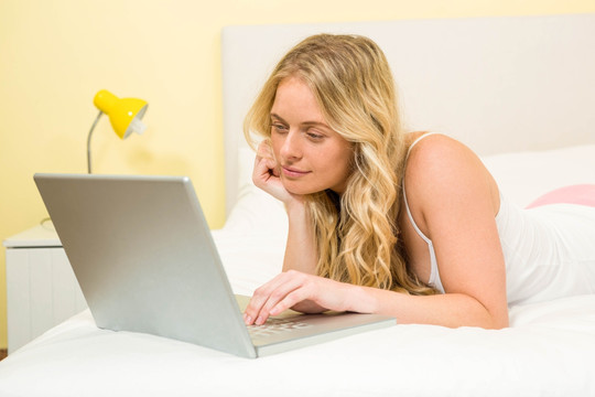 趴在床上使用笔记本电脑的女人