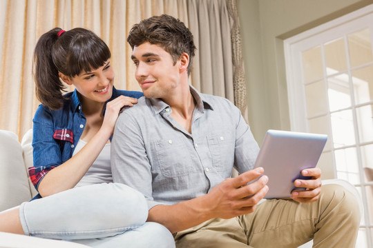 坐在沙发上用平板电脑的年轻夫妇