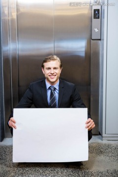 在电梯门口拿着海报的男商人