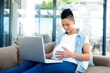 坐在沙发上使用笔记本电脑的孕妇