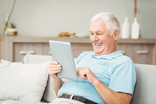 微笑的老人坐在沙发上用平板电脑