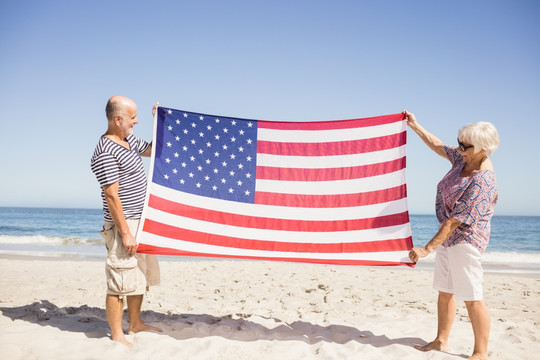 拿着美国国旗的站在海边的老夫妇