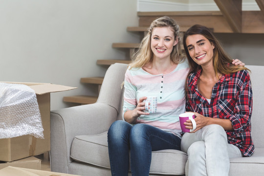 年轻女人和朋友坐在沙发上喝咖啡