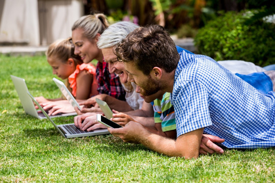 趴在草坪上用数码产品的家人