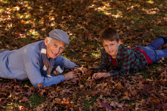 祖父和孙子趴在秋天的叶子上