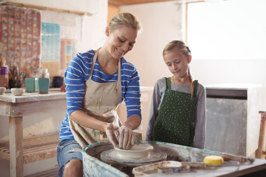 在协助女孩做陶器的女人