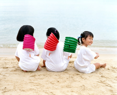 三个孩子坐在沙滩上拿着中国灯笼