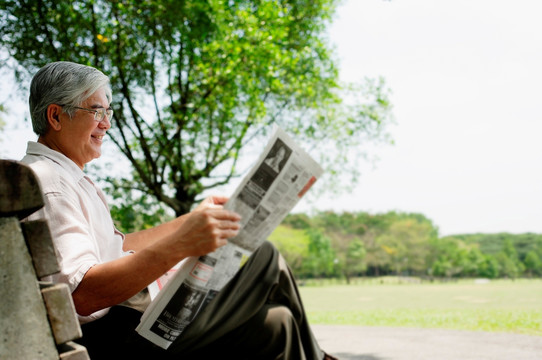 高级男子坐在长椅上看报纸
