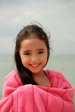年轻女孩在海滩裹着粉红色的毛巾