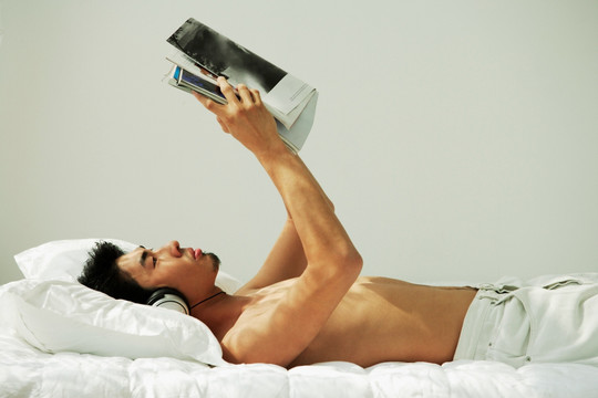 年轻人躺在床上看书和听音乐