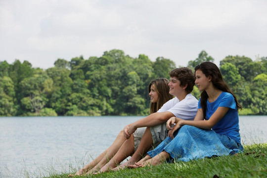 三个少年坐在湖边的草地上