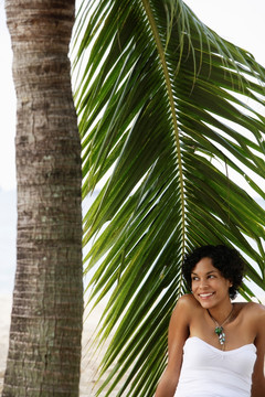 年轻女子坐在棕榈树下微笑