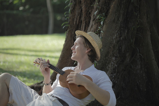 年轻人在树下玩尤克里里琴