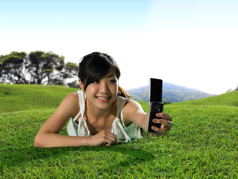 趴在草坪上使用手机自拍的女人