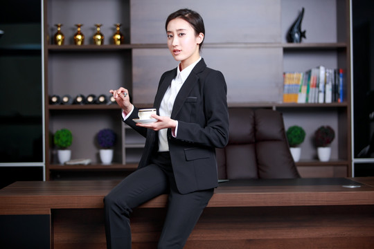 拿着一杯咖啡坐在老板桌上的女人