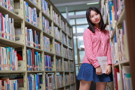 微笑的女大学生靠在书柜上