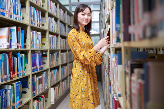 微笑的女学生站在大学图书馆里看书