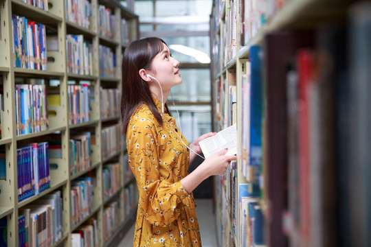 女学生拿着书看着图书架