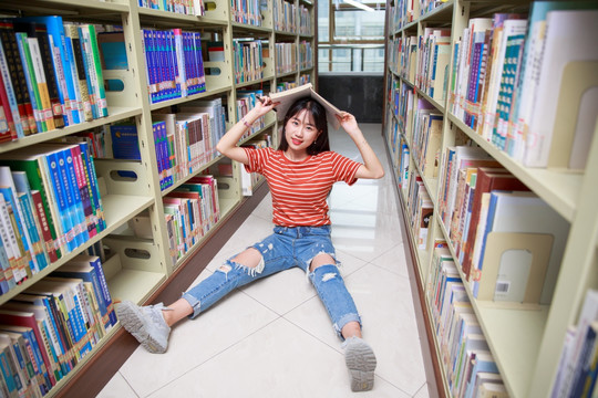 女学生坐在图书馆地上拿书盖着头