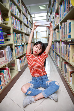 女学生盘腿坐在地上高举着书本