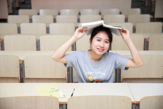 微笑的女学生把书本盖在头上 