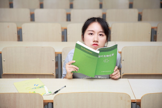 女学生拿着书籍坐在大学教室里