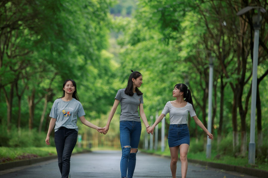 女学生手拉手在林荫道上走着