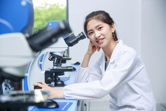 微笑的女学生坐在显微镜旁
