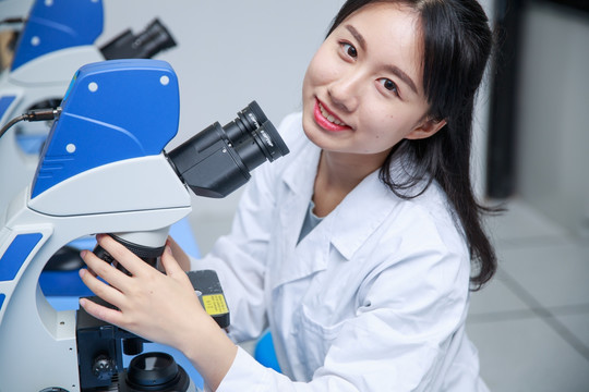 微笑着使用显微镜的女学生