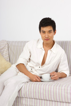 年轻男人躺在沙发上喝咖啡