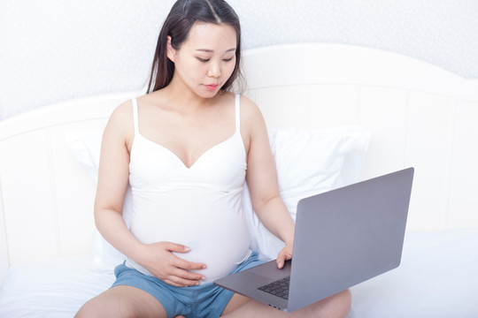 孕妇坐在床上使用笔记本电脑